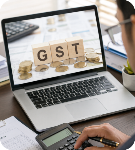 Laptop displaying GST blocks alongside coins, tax documents, and a calculator for online GST return filing